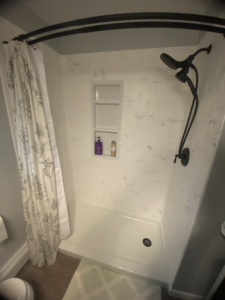 “Completed Samuel Mueller solid surface shower conversion with marble-look finish, niche, and matte black fixtures in Lancaster PA bathroom”